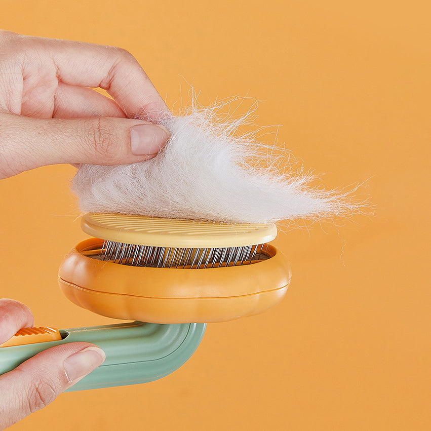 Hand holding Cute Pumpkin Pet Grooming Comb with loose fur on it against an orange background.